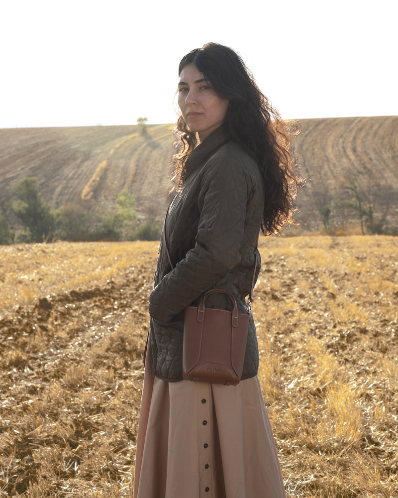 Woman standing in a field wearing a brown leather bag