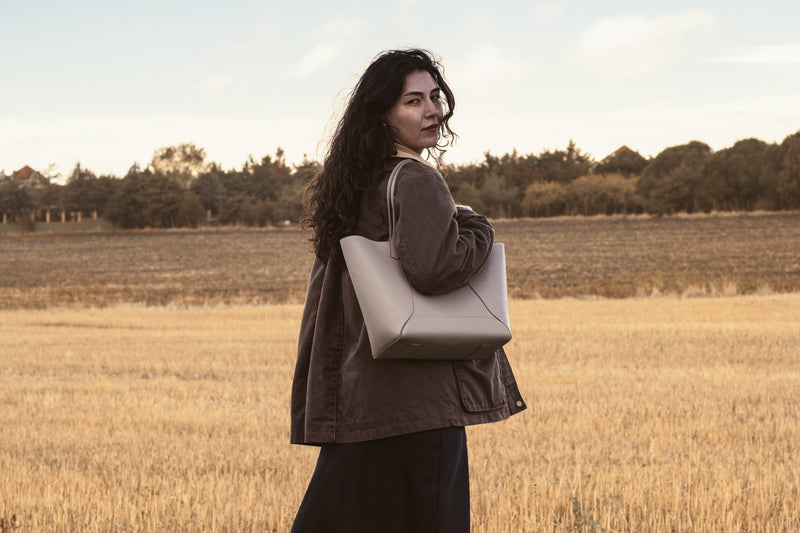 Woman holding a beige  tote bag in a field during sunset