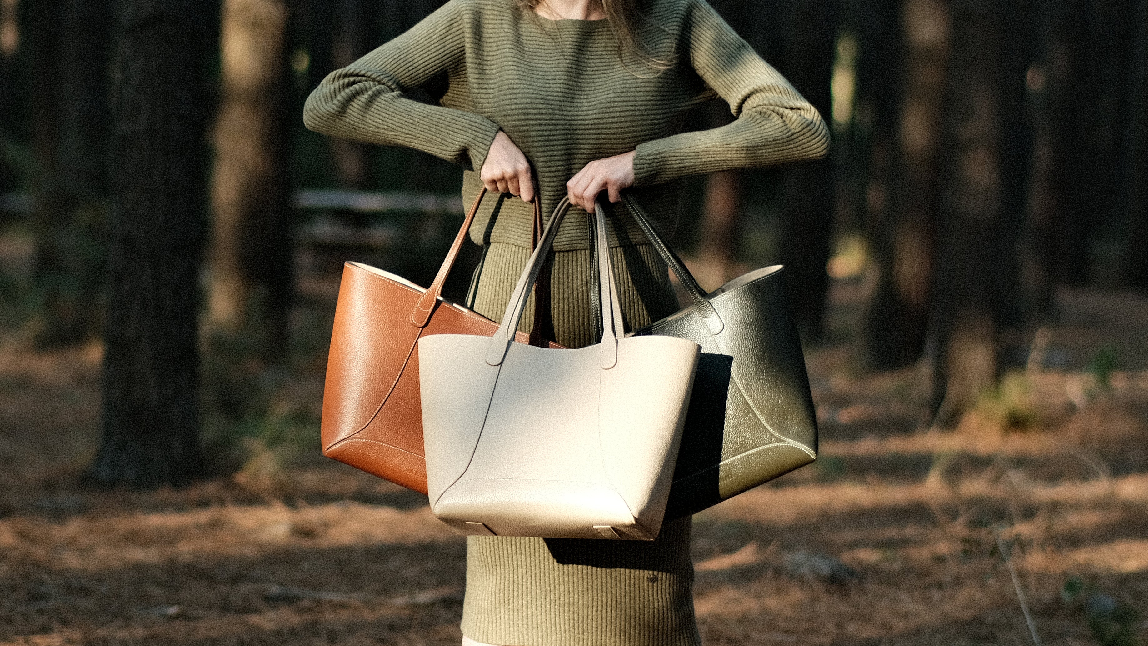 Person holding three tote bags in a forest setting