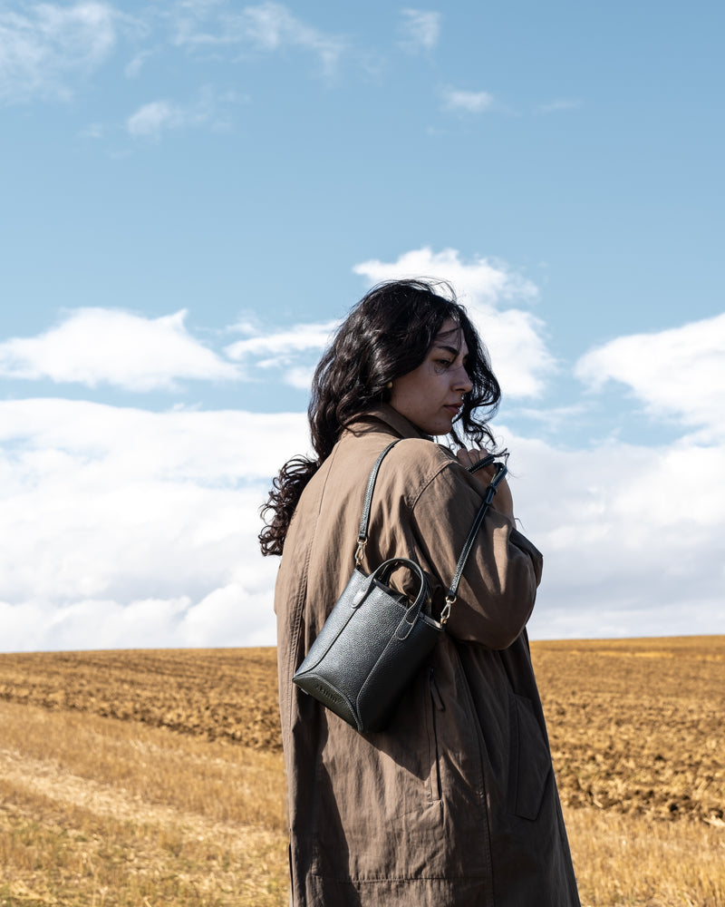 Woman standing in a field with a dark green leather hand bag